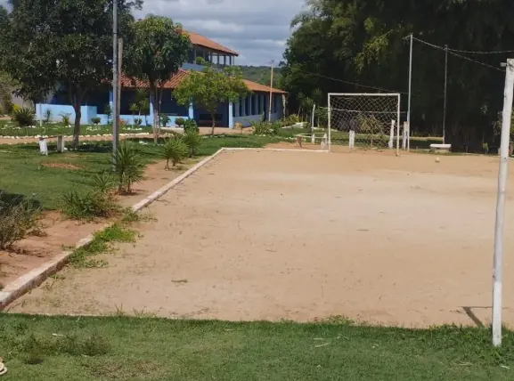 Clínica de Recuperação em Divinópolis - MG Campo de terra batida com uma trave ao fundo, gramado em volta e um sobrado azul à esquerda